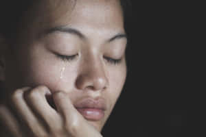 一個女人在昏暗的燈光下閉著眼睛哭泣。 — 悲傷女孩 壁紙