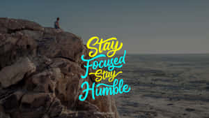 人坐在懸崖邊緣俯瞰沙漠，帶有「Stay Focused Stay Humble」文字。 — 吸血鬼家庭屍篇 壁紙