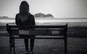 人坐在水邊繪有「Miss you」的長椅上 — 孤獨 壁紙