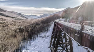 人坐在雪鐵路橋上，俯瞰冬季山脈和陽光。 — 冬季風景 壁紙