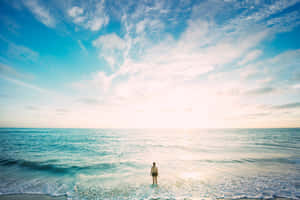 日落時分，一個人站在淺海水中，廣闊的天空和溫柔的波浪。 — 海景 壁紙