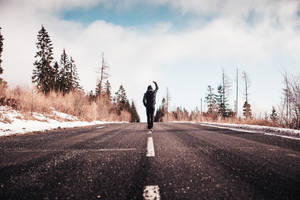 一個人舉起一隻手臂，走在穿過冬季森林的積雪道路上。 — 動力 壁紙