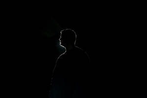 一個人的剪影，由一道光束在黑暗背景上勾勒出輪廓。 — 純黑 壁紙