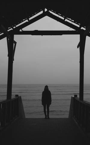 一個人獨自站在碼頭盡頭，眺望平靜、霧濛濛的海洋。 — 剪影 壁紙