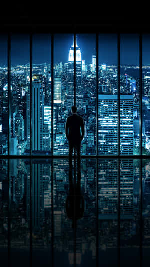 剪影中的人透過窗戶凝視著夜晚發光的城市，下方有完美的倒影。 — 舊金山 iPhone 壁紙