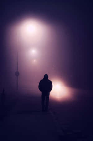 在發光的燈光下，夜間霧氣瀰漫的城市街道上獨自行走的人的剪影。 — 霓虹紫 壁紙