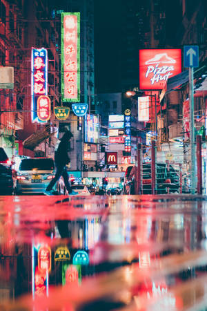 行人穿過霓虹燈照亮的濕漉漉的夜晚街道，倒影閃爍 — 香港 壁紙