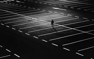 一個孤獨的人影在夜晚獨自走在廣闊的空停車場上。 — 獨自一人 壁紙