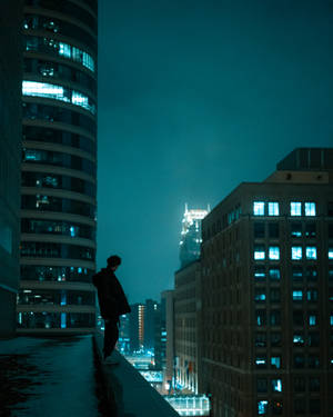 一個人站在屋頂上俯瞰夜晚城市的剪影。 — 美學天空 壁紙