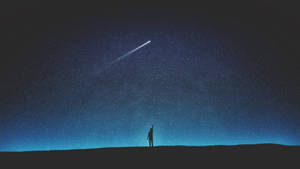 一個人在夜晚站在山丘上，伸手去抓星空中的流星。 — 剪影 壁紙