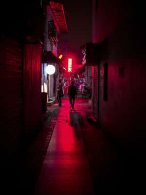 夜晚，一個人在潮濕路面上、紅色霓虹燈照亮的小巷中行走。 — 城市燈光 壁紙