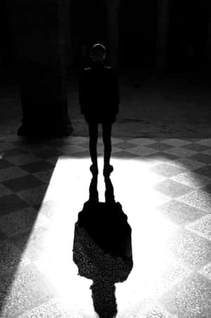 一個人站在黑暗的大廳中，在棋盤格地板上投下強烈的影子。 — 剪影 壁紙