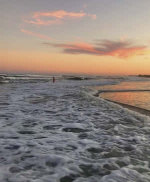在色彩繽紛的日落中，一個人站在海浪中。 — 海灘度假 壁紙