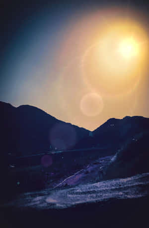 一個人在山路上行走，太陽在山峰後落下，伴隨著鏡頭光暈。 — 海灘日落 壁紙