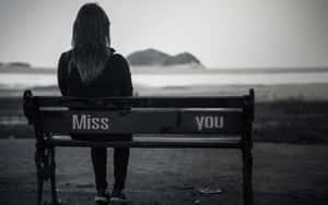 一個人獨自坐在水邊的長椅上，上面寫著「Miss you」。 — 孤獨 壁紙