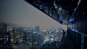 一個人獨自坐在玻璃屋頂上，俯瞰夜晚燈火通明的城市。 — 電玩遊戲 GIF 壁紙