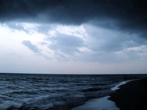 一個孤獨的人在暮色中沿著暴風雨的海灘行走，頭頂有烏雲。 — 美學雲朵 壁紙