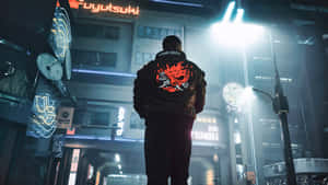 穿著火焰外套的人站在霓虹燈照亮的城市夜景中。 — 電馭叛客2077 壁紙
