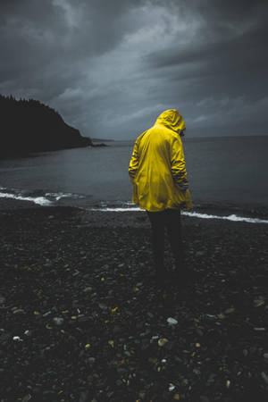 暴風雨中，穿著黃色雨衣的人獨自站在岩石海灘上。 — 海灘 壁紙
