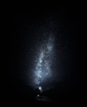 穿黃色外套的人晚上用手電筒照射銀河星星。 — 黑夜 壁紙