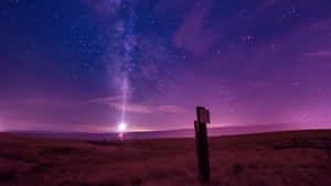 一個人在沙漠中，站在可見銀河的紫色星空下。 — 月夜星空 壁紙
