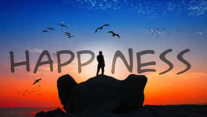 日落時分懸崖上一個人的剪影，鳥兒飛翔，並顯示了happiness這個詞。 — 喜悅 壁紙