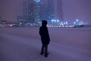 人站在雪中，面向夜晚燈火通明的城市天際線。 — 霓虹車 壁紙
