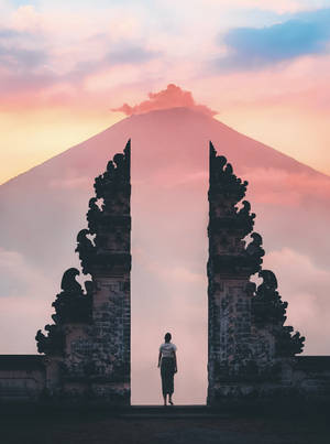 人站在古老的大門之間，看著日落時霧氣繚繞的火山。