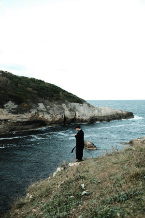 穿黑色外套的人獨自站在海邊懸崖邊 — 海景 壁紙