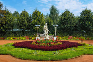 花園中的雕像，周圍環繞著五顏六色的花朵和綠樹，在藍天下。 — 花園 壁紙