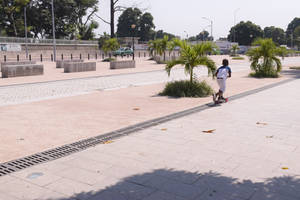 小孩在鋪砌廣場上騎滑板車，有棕櫚樹和長椅 — 剛果 壁紙