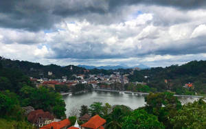 多雲的天空下，一個湖邊小鎮被綠色山丘環繞的風景如畫的景色。 — 斯里蘭卡 壁紙