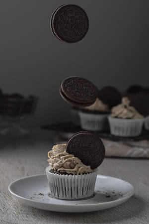 巧克力紙杯蛋糕上懸浮著 Oreo 餅乾，放在白色盤子上。 — 杯子蛋糕 壁紙