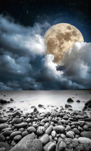 月亮在夜間從雲層後升起，照耀著岩石海灘，星星清晰可見。 — 海灘 壁紙