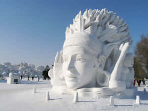 在雪地公園裡，一個戴著頭飾的臉部大型雪雕，旁邊有遊客。 — 冰龍 壁紙