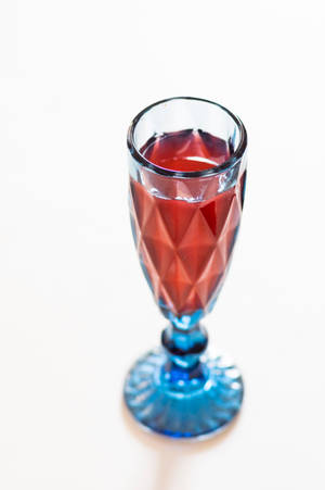 白色表面上一個帶有紅色液體的藍色切面玻璃杯。 — 透明 壁紙