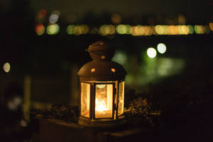 一個點亮的燈籠，帶有星星鏤空，在夜晚的城市景觀中發光。 — 昏暗 壁紙