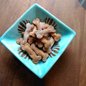 綠松石碗，木質表面上放有骨形狗零食。 — 狗狗藝術 壁紙