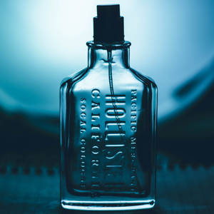 帶有浮雕文字的復古玻璃古龍水瓶，背景為藍色漸變。 — Hollister 壁紙