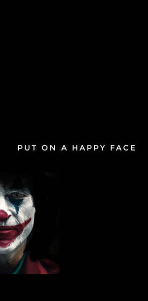 一個帶有紅色嘴唇和藍色眼淚的可怕小丑，從黑暗中的「put on a happy face」文字下方向上凝視。 — 黑白小丑 壁紙
