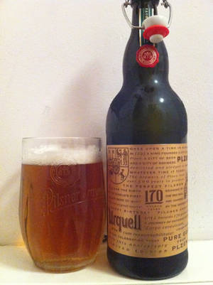 一瓶Pilsner Urquell啤酒旁邊放著一杯裝滿琥珀色啤酒和泡沫的玻璃杯。 — 啤酒 壁紙