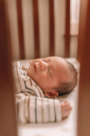 一個在木製嬰兒床中穿著條紋睡衣睡覺的新生嬰兒。 — 小莫娜 壁紙