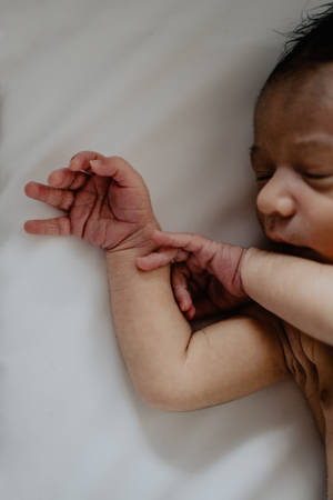 一個睡覺的新生嬰兒，一隻手繞著手腕放在白色表面上。 — 小莫娜 壁紙