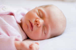 一個在白色毯子上穿著粉紅色連身衣睡覺的新生嬰兒。 — 小莫娜 壁紙