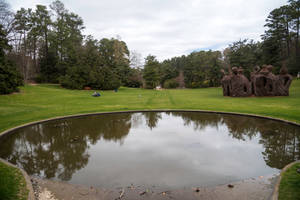 公園裡一個寧靜的池塘，有一個大型樹枝雕塑，人們在草地上放鬆。 — 花園 壁紙