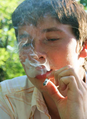 年輕男子在戶外明亮的陽光下吸煙，身後有綠色樹木。 — 抽菸 壁紙