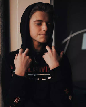 年輕男子穿黑色連帽衫閉眼調整帽子室內 — 黑執事 壁紙