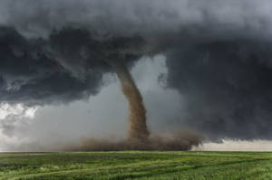 在暴風雨的天空下，一個巨大的龍捲風在綠色田野上揚起塵土。 — 凋零風暴 壁紙