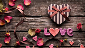 心形禮物盒和粉紅色糖字母拼出 love 在木桌上，伴有玫瑰花瓣。 — 美學愛心 壁紙