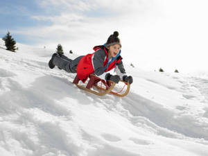 孩子穿著紅色外套和針織帽在雪坡上滑雪橇 — 冬季 壁紙